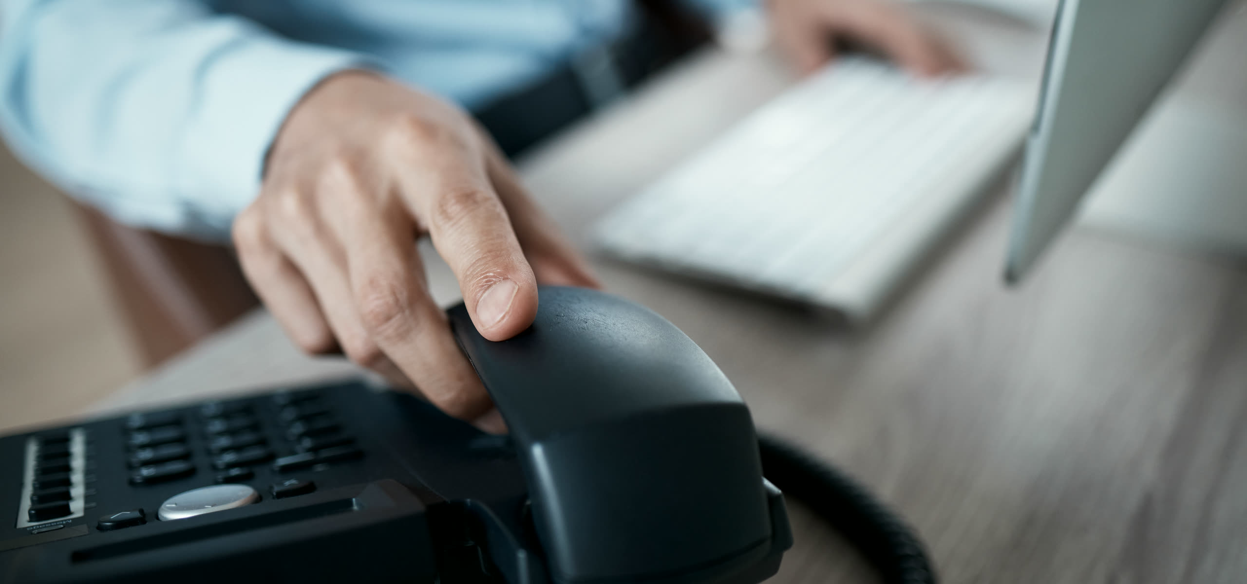 A small office desk with a handset lifted off its cradle, a laptop open on a list of enquiries and a notepad of scribbled callbacks.