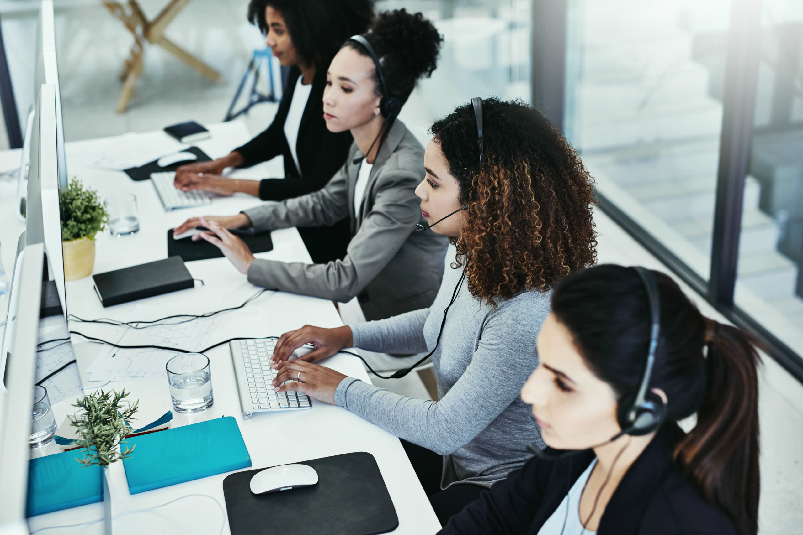 A claims handler at a desk in an open-plan office, headset on, one screen showing a policy schedule and the other an open claim record.