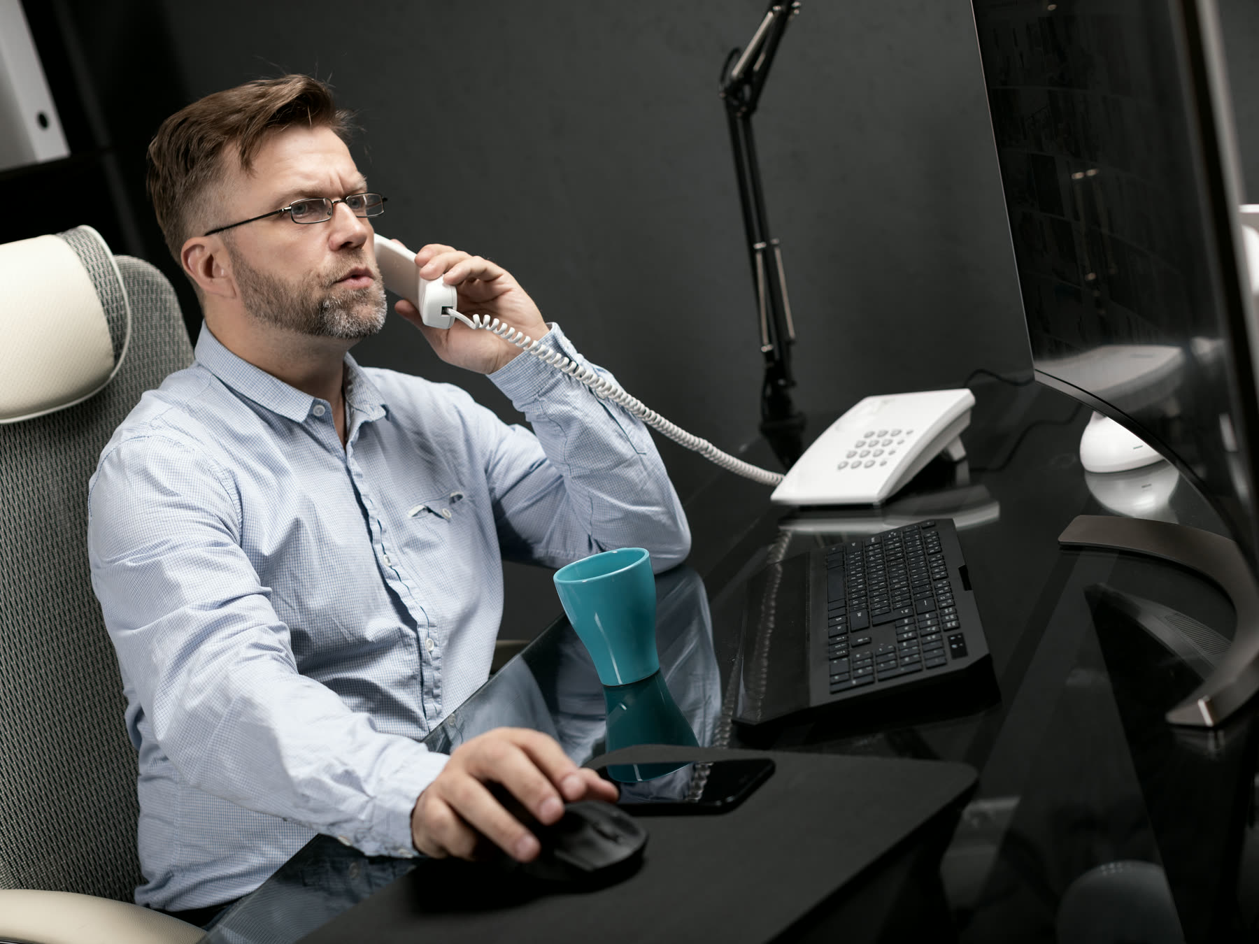 A desk telephone in use beside a working screen
