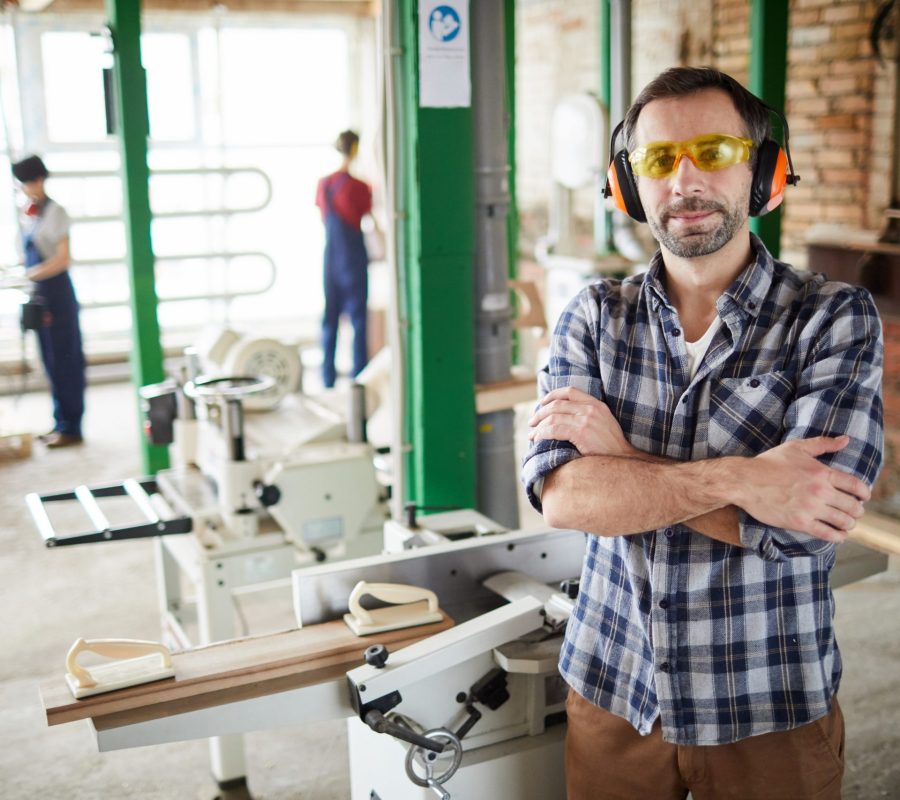 Modern Carpenter Posing in Workshop Waist up portrait of confident mature carpenter standing with arms crossed in workshop, copy space
